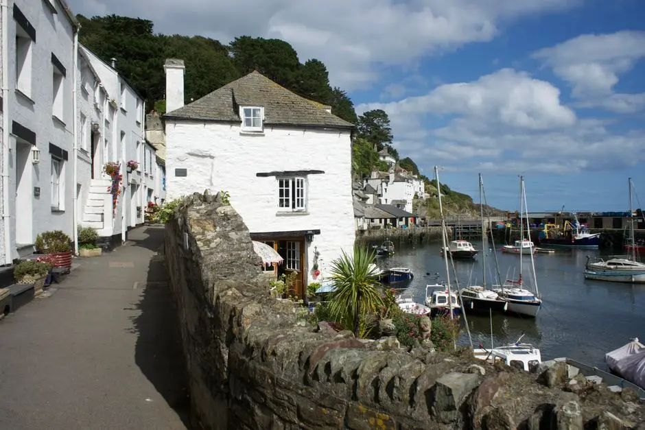 Picturesque scene of Polperro harbour with boats and historic cottages under a bright sky.